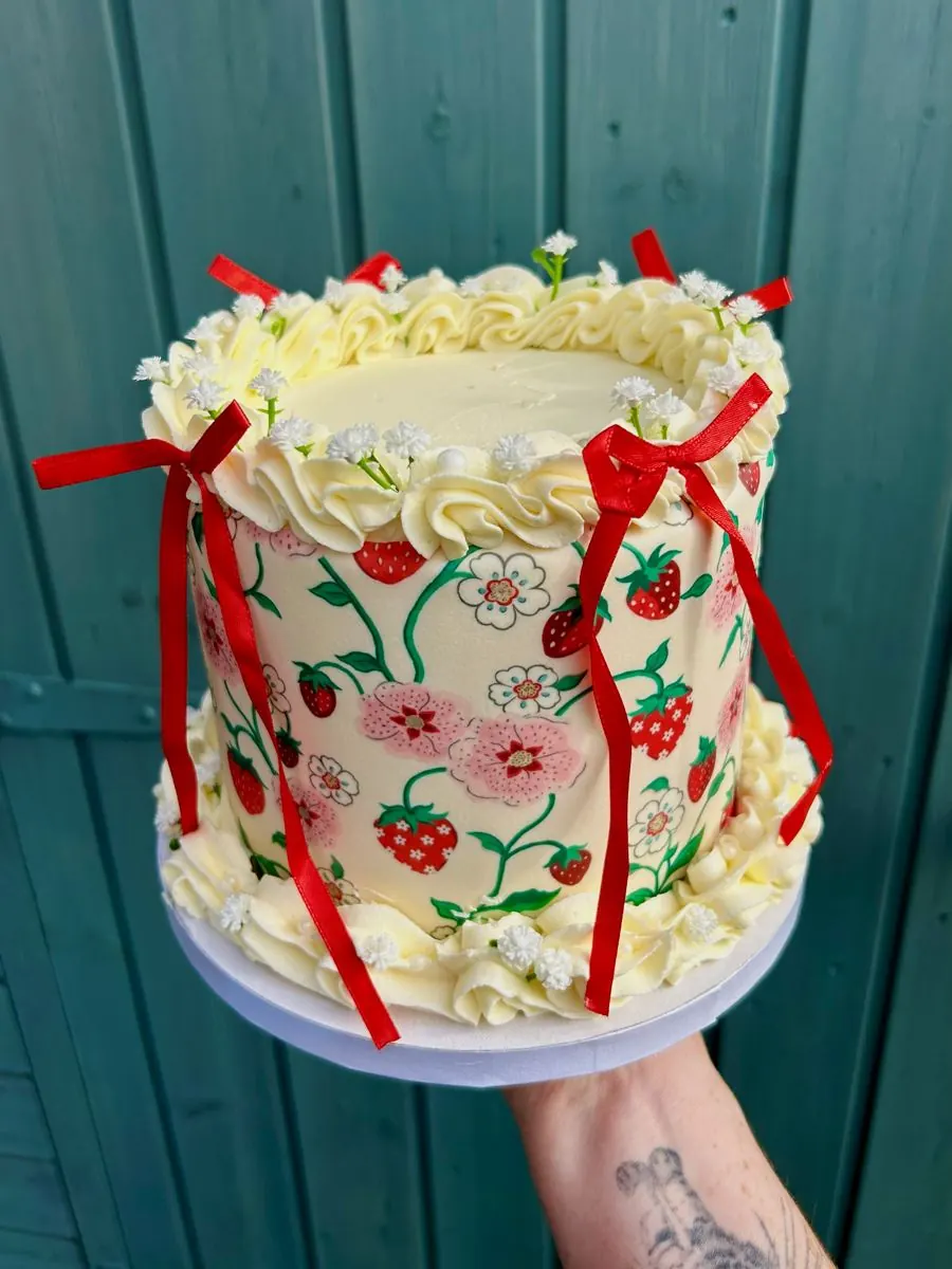 Cream cake painted with strawberries and flowers, tied with red ribbon bows